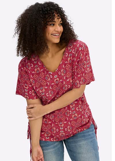 Ein Model trägt ein rot-koralle-gemusterts T-Shirt mit Alloverprint , Flügelärmeln und V-Ausschnitt