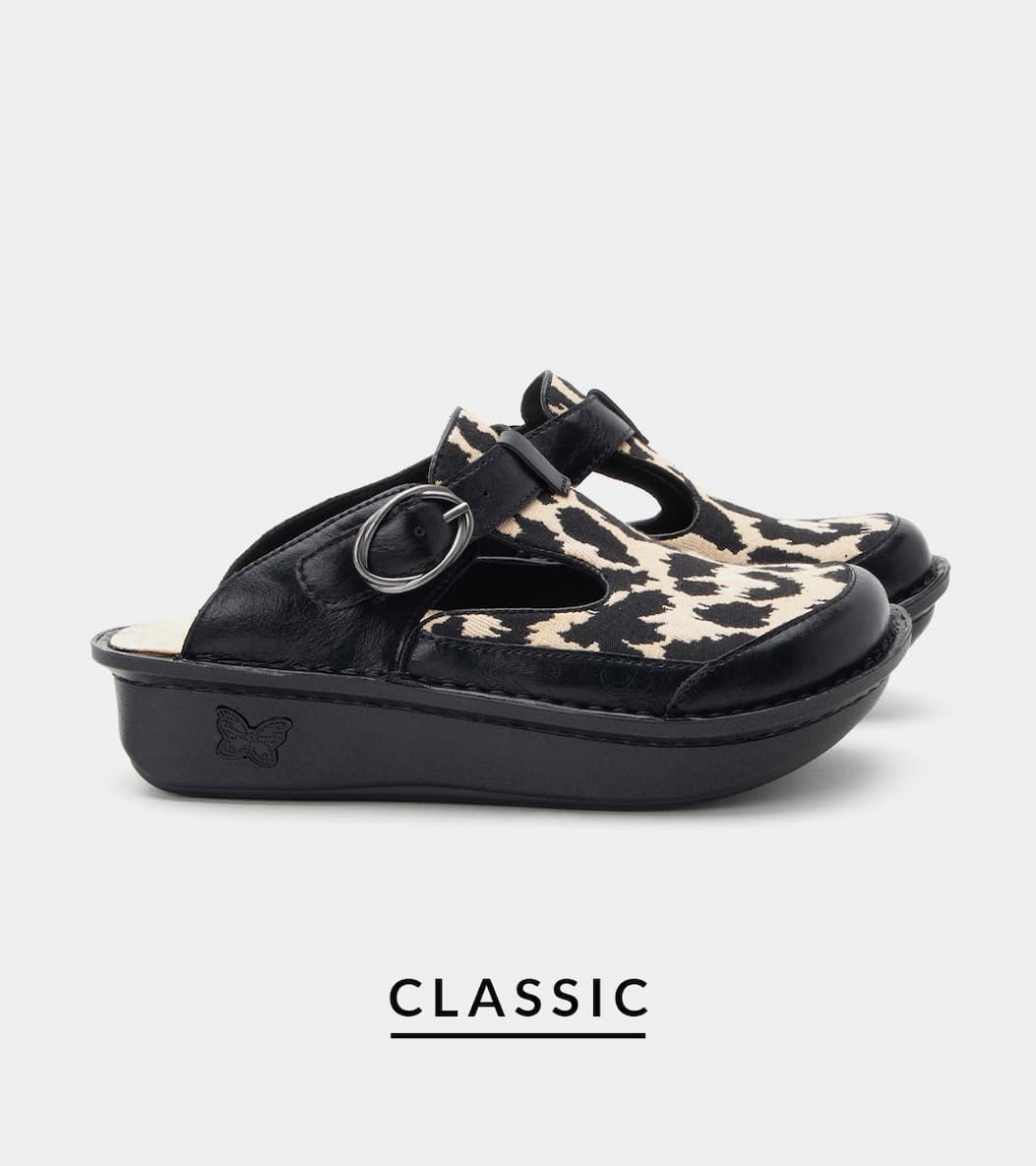 Pair of black leather and animal print clog-style shoes with a cut out opening detail and buckle strap with an oval silver buckle. Product name "CLASSIC" printed beneath on a light gray background.