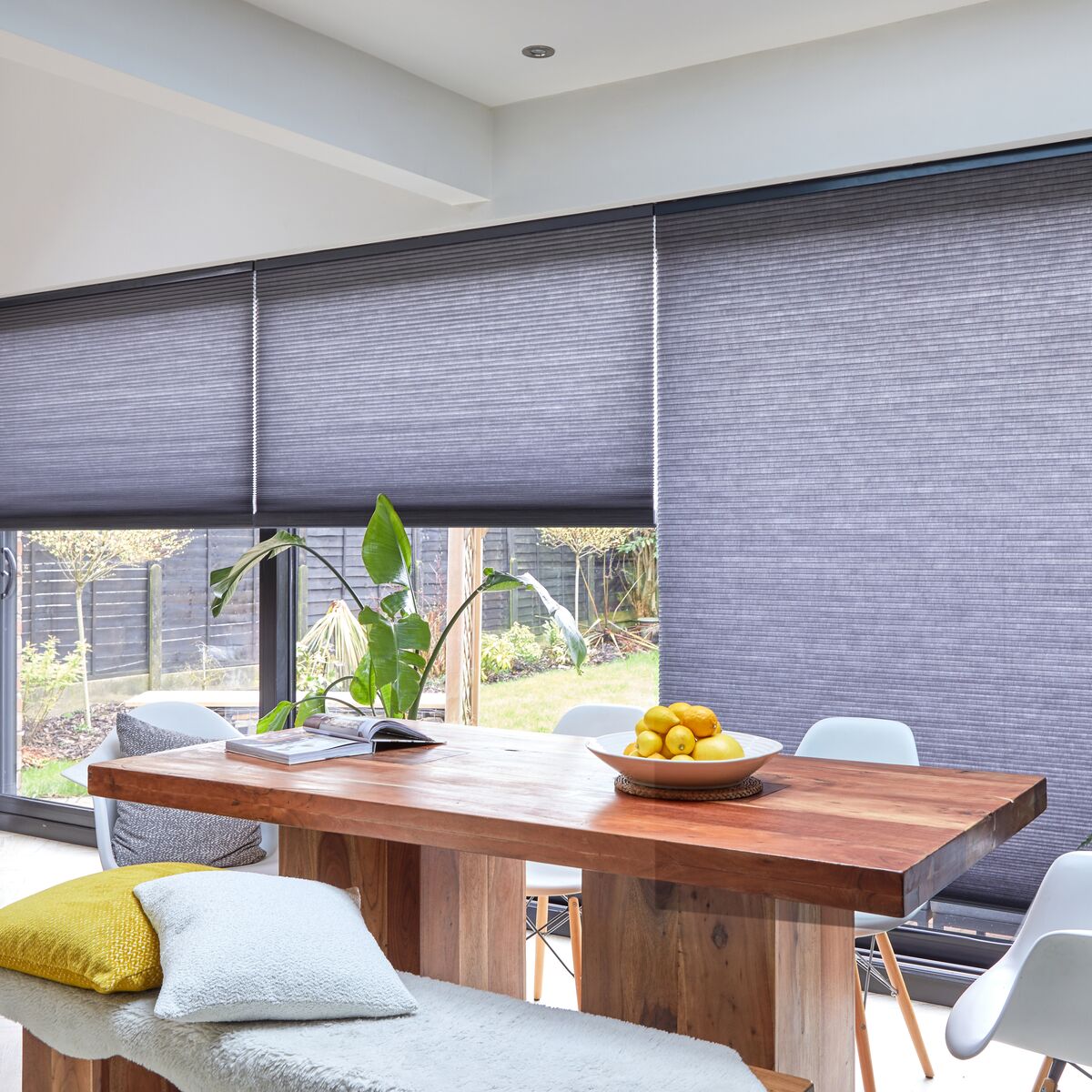 Duette blinds filter daylight across wide patio doors, framing a bright dining area with a wooden table and garden views.