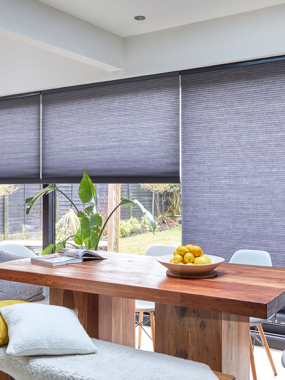 Duette blinds filter daylight across wide patio doors, framing a bright dining area with a wooden table and garden views.