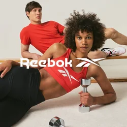Dos adultos jóvenes con ropa deportiva roja haciendo ejercicio; la mujer sostiene una mancuerna tumbada en el suelo, el hombre se reclina sobre una barra de madera.
