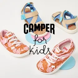 Dos pares de zapatos infantiles sobre plataformas circulares: uno naranja con patrones rosa y cordones blancos, y sandalias beige con acentos azules.
