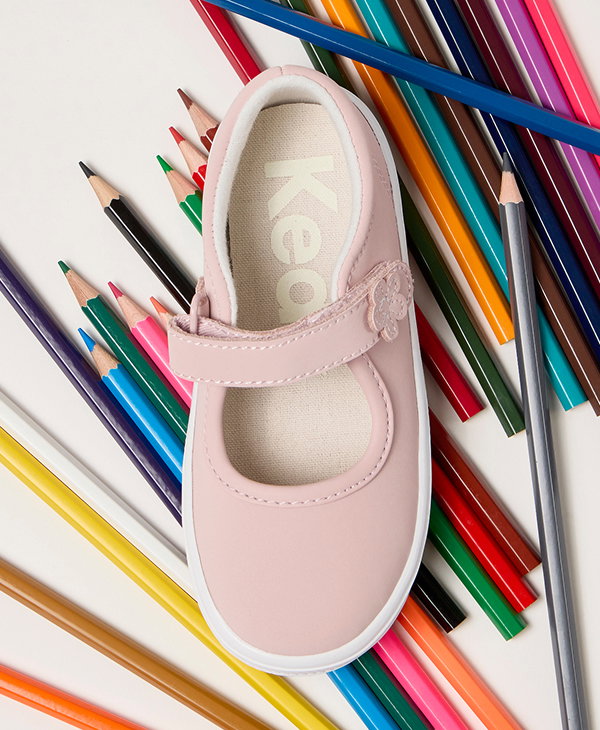 A top-down view of the Little Kids’ Ella Mary Jane sneakers in light pink sitting on top of an array of bright colored pencils.