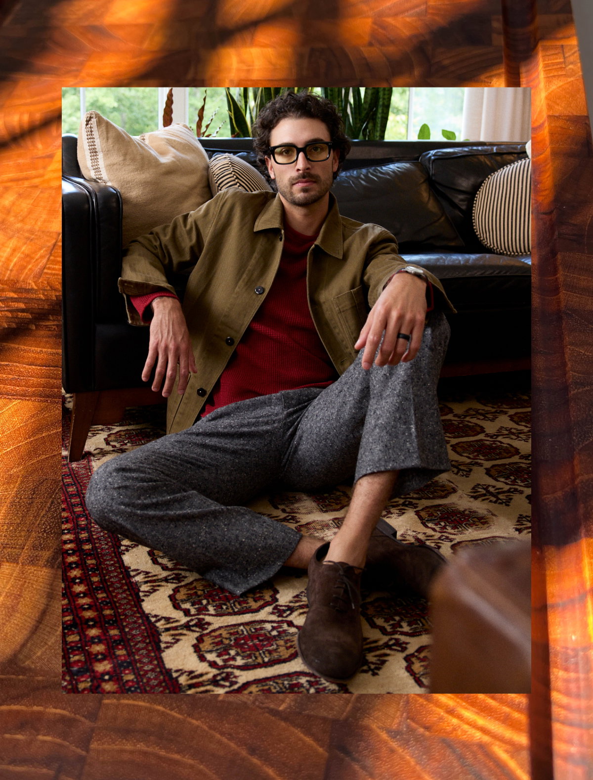 Man wearing a green jacket with black buttons over a red sweater in a rustic cabin