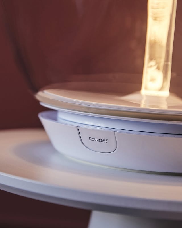 Close-up of a white modern table lamp base with a glowing filament bulb and Artemide logo on a round side table