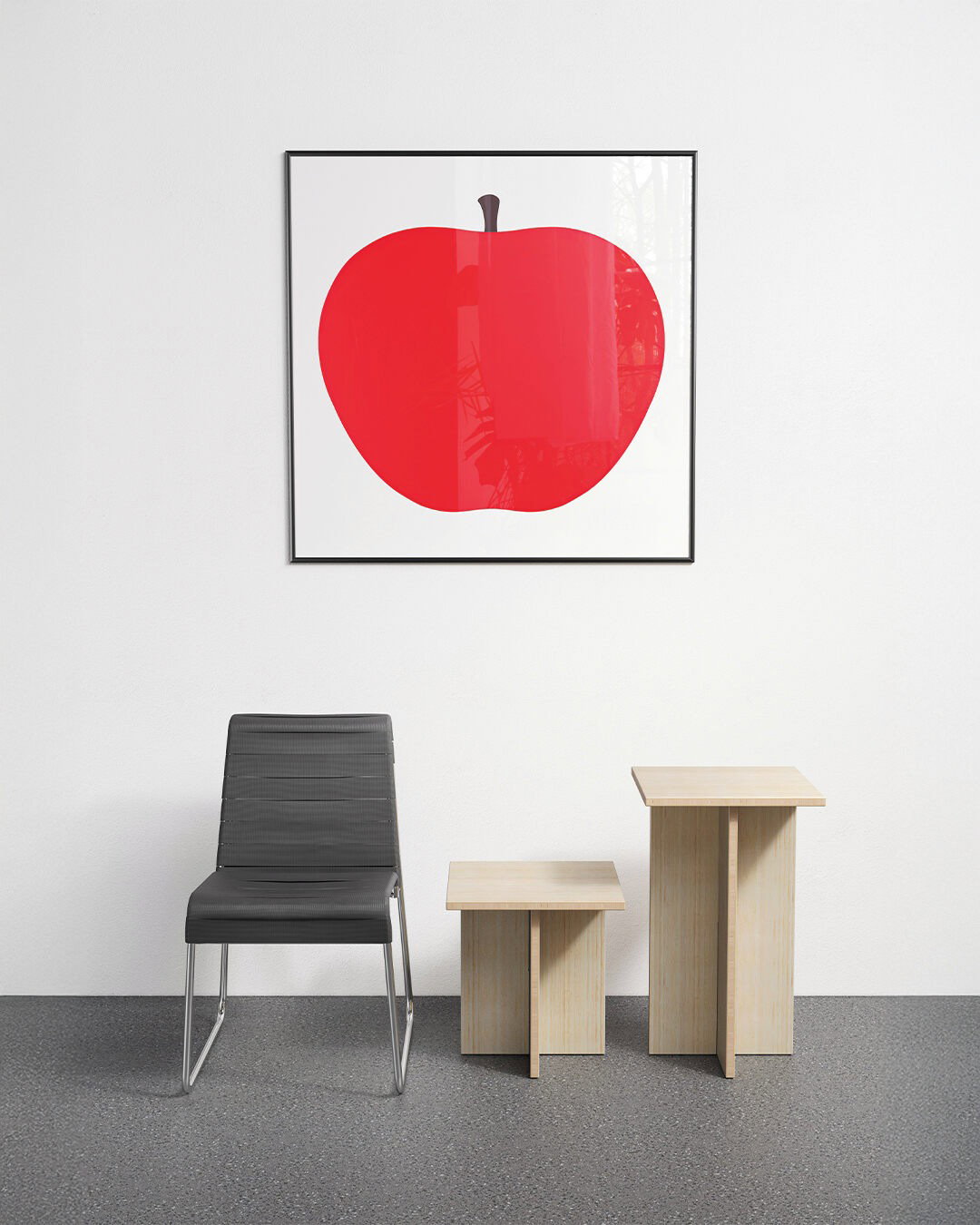 Minimalist room with framed red apple print on white wall above a black modern chair and two light-wood nesting side tables on a grey floor