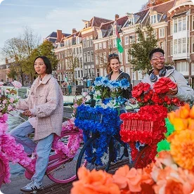 Three friends on bikes decorated with colorful flowers along a canal.