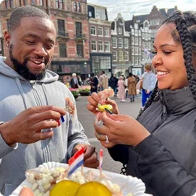 A couple sampling Dutch street food snacks at an outdoor market.