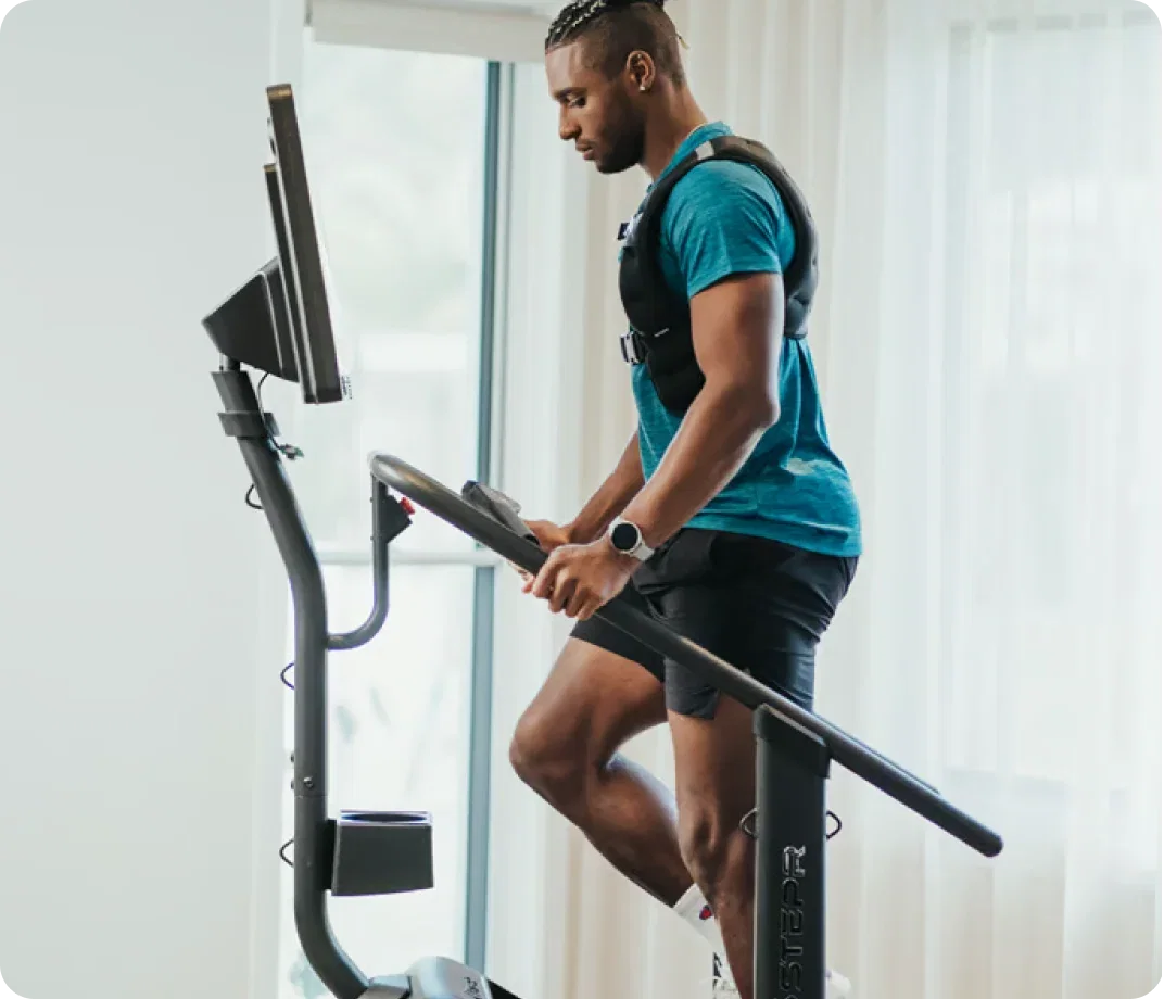 Man climbing on a STEPR machine while wearing a weighted vest.