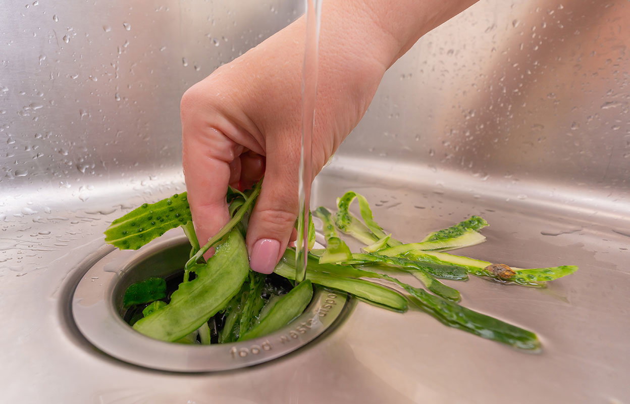 A hand putting food waste down a garbage disposal