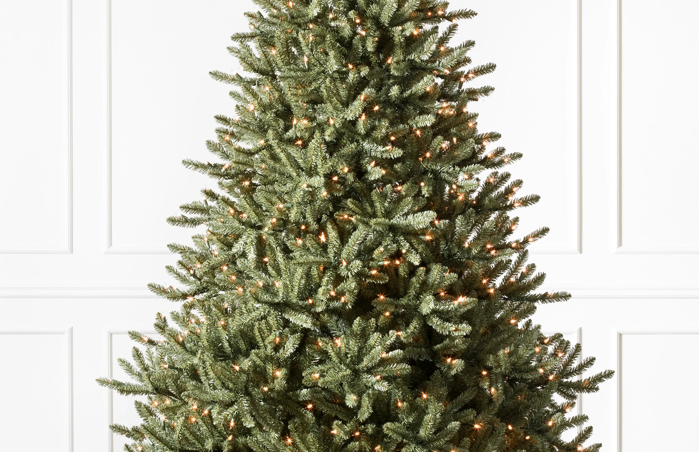 Close-up of a pre-lit artificial Christmas tree with dense green branches and warm white lights.