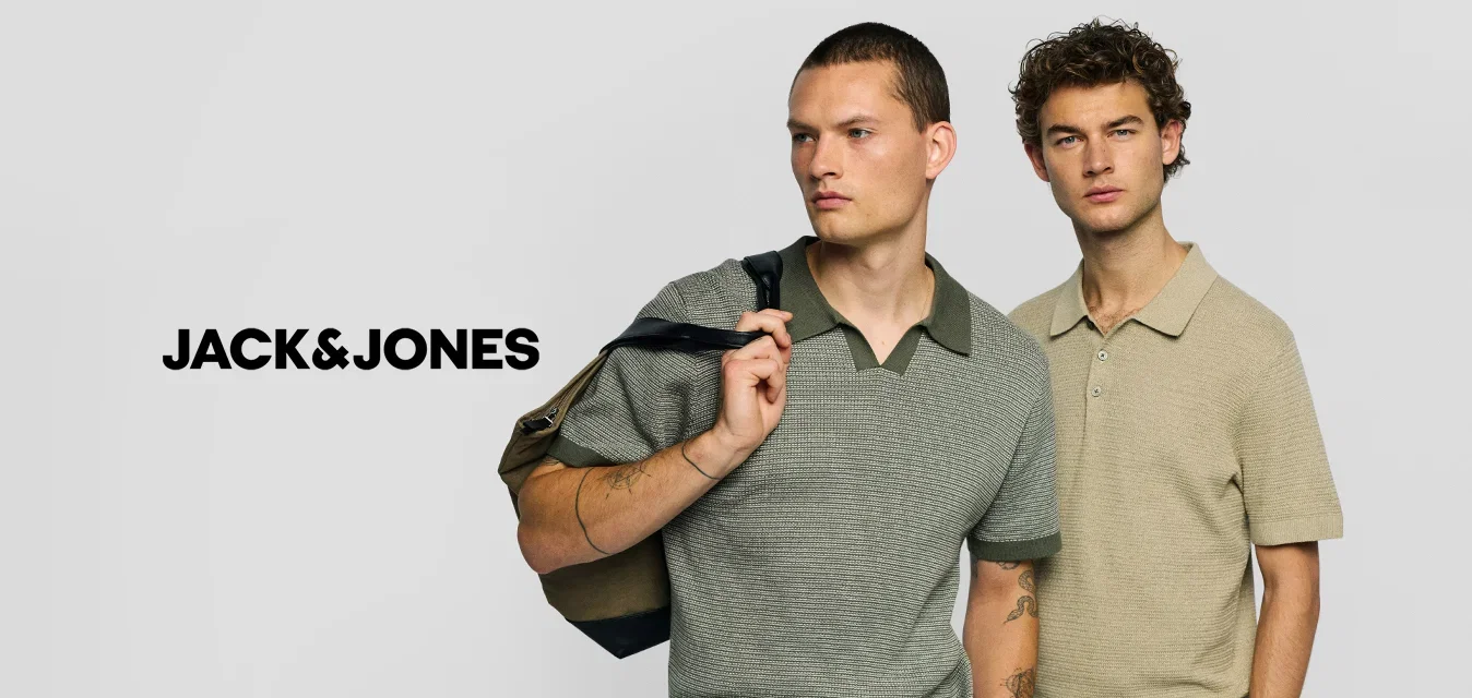 Twee mannen staan naast elkaar met gebreide poloshirts met korte mouwen, een grijze met groene kraag en een tas over de schouder, de andere beige met handen in de zakken.
