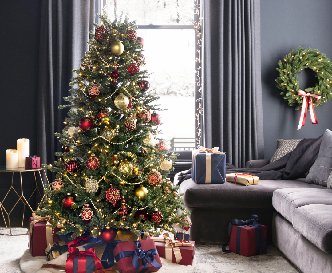 A front room with presents scattered around and a Christmas tree with red and gold ornaments. 