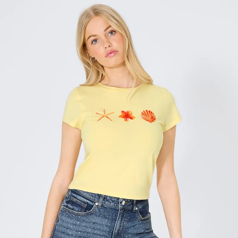 Frauenmodel trägt gelbes T-Shirt mit maritimem Aufdruck, blaue Jeans mit Punkten, Vorderansicht