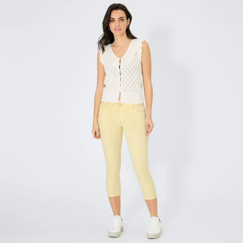 Frauenmodel trägt ärmelloses, cremefarbenes Stricktop mit Lochmuster, gelbe 7/8-Hose, Vorderansicht