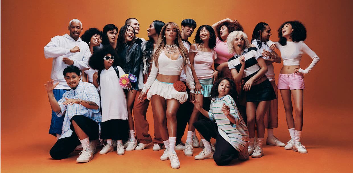 Community of people wearing Reebok Classics sneakers pose together against an orange backdrop.