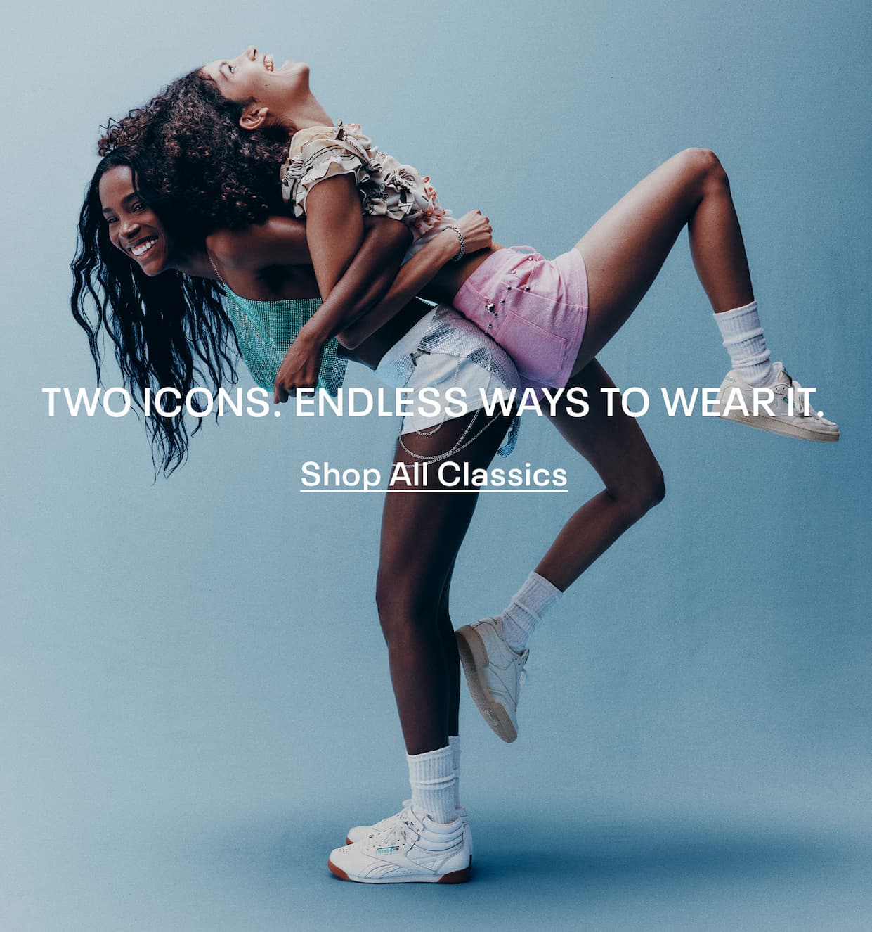 Two people wearing Reebok Classics apparel and sneakers pose together against a blue backdrop. Text reads: “TWO ICONS. ENDLESS WAYS TO WEAR IT. Shop All Classics.”
