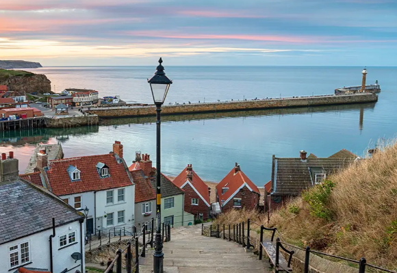 View of a coastal town with colourful houses, a pier, and calm waters under a pastel sky.
