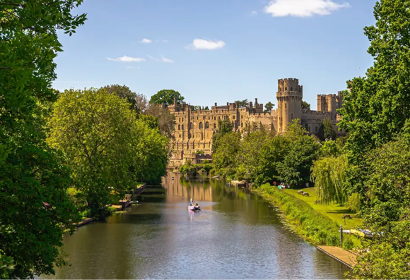 A scenic view of a river with a castle in the background, surrounded by lush greenery and blue skies.