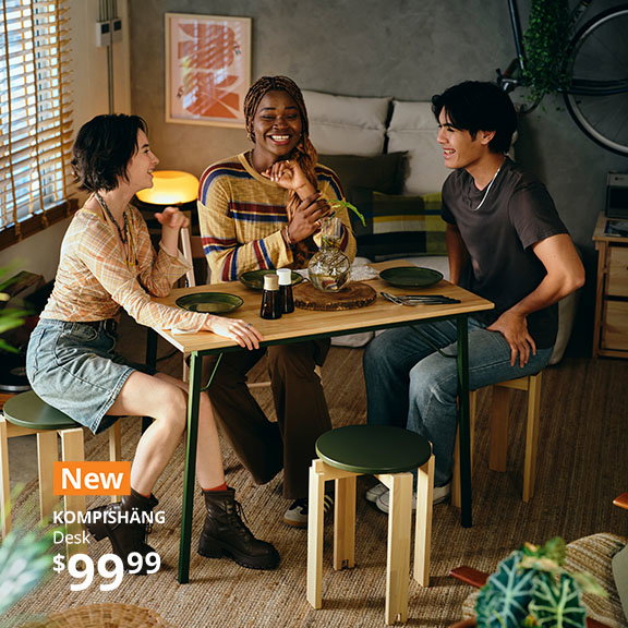 Three young adults sit at the Live on the move with the KOMPISHÄNG desk table.