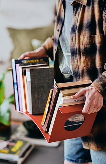 A person carrying the KOMPISHÄNG book-end full of books through their apartment.