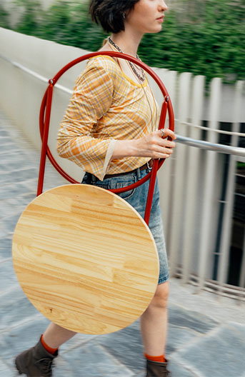 A woman cerrying a folded KOMPISHÄNG side table on her shoulder.