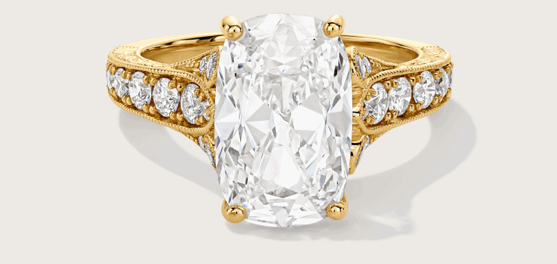 Yellow gold cushion-cut engagement ring, with four-prong setting and diamonds along the band.