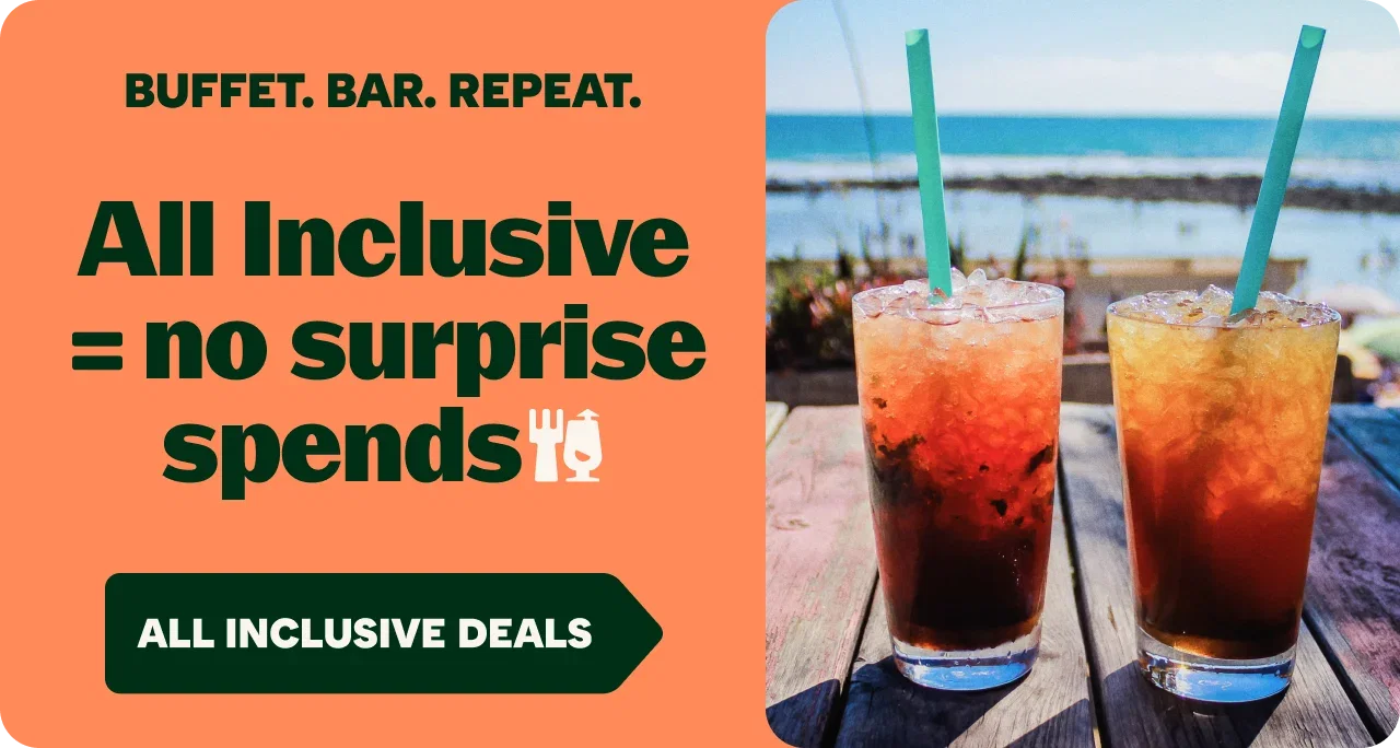 Promotional travel advert with the text “BUFFET. BAR. REPEAT.” and “All Inclusive = no surprise spends,” alongside a button reading “ALL INCLUSIVE DEALS.” On the right, two iced drinks with straws sit on a wooden table overlooking a sunny beach and blue sea, highlighting the value of an all-inclusive holiday.