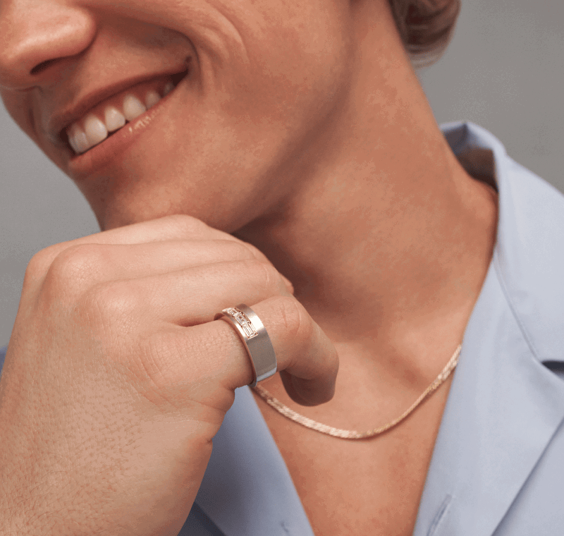 Close-up of a man in a blue shirt, yellow gold chain necklace and gold and diamond signet ring on pinkie.