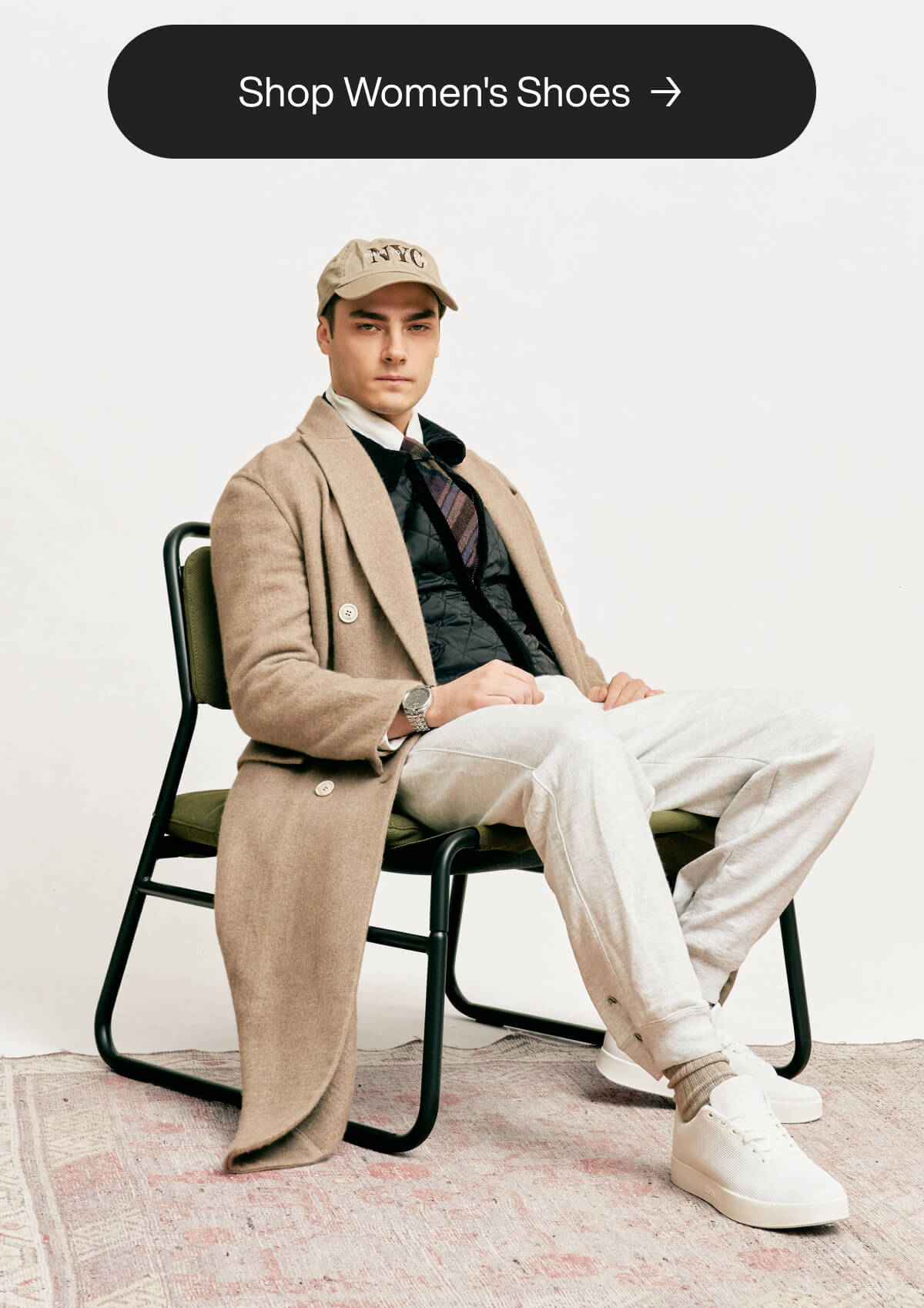 "Man in beige coat and cap sits on a chair, wearing white sneakers. Text above: "Shop Women's Shoes"."