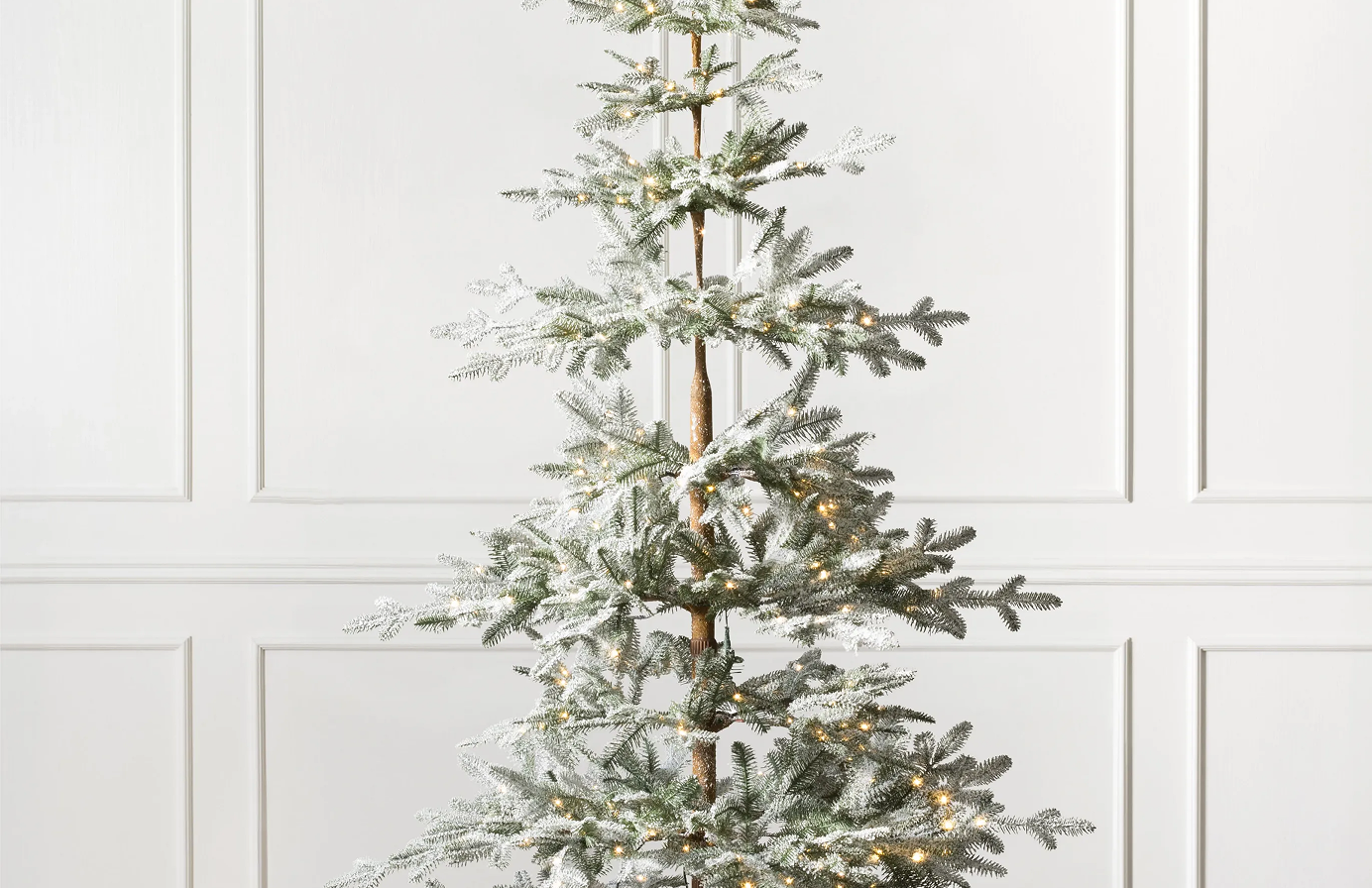 Sparse pre-lit flocked Christmas tree with snow-dusted branches and a natural trunk.
