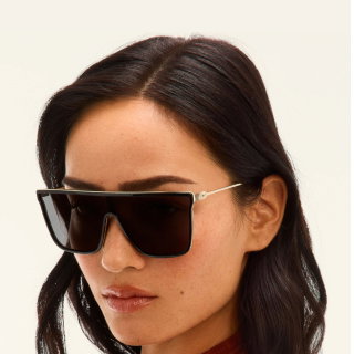 Image of woman wearing black shield sunglasses with gold frames