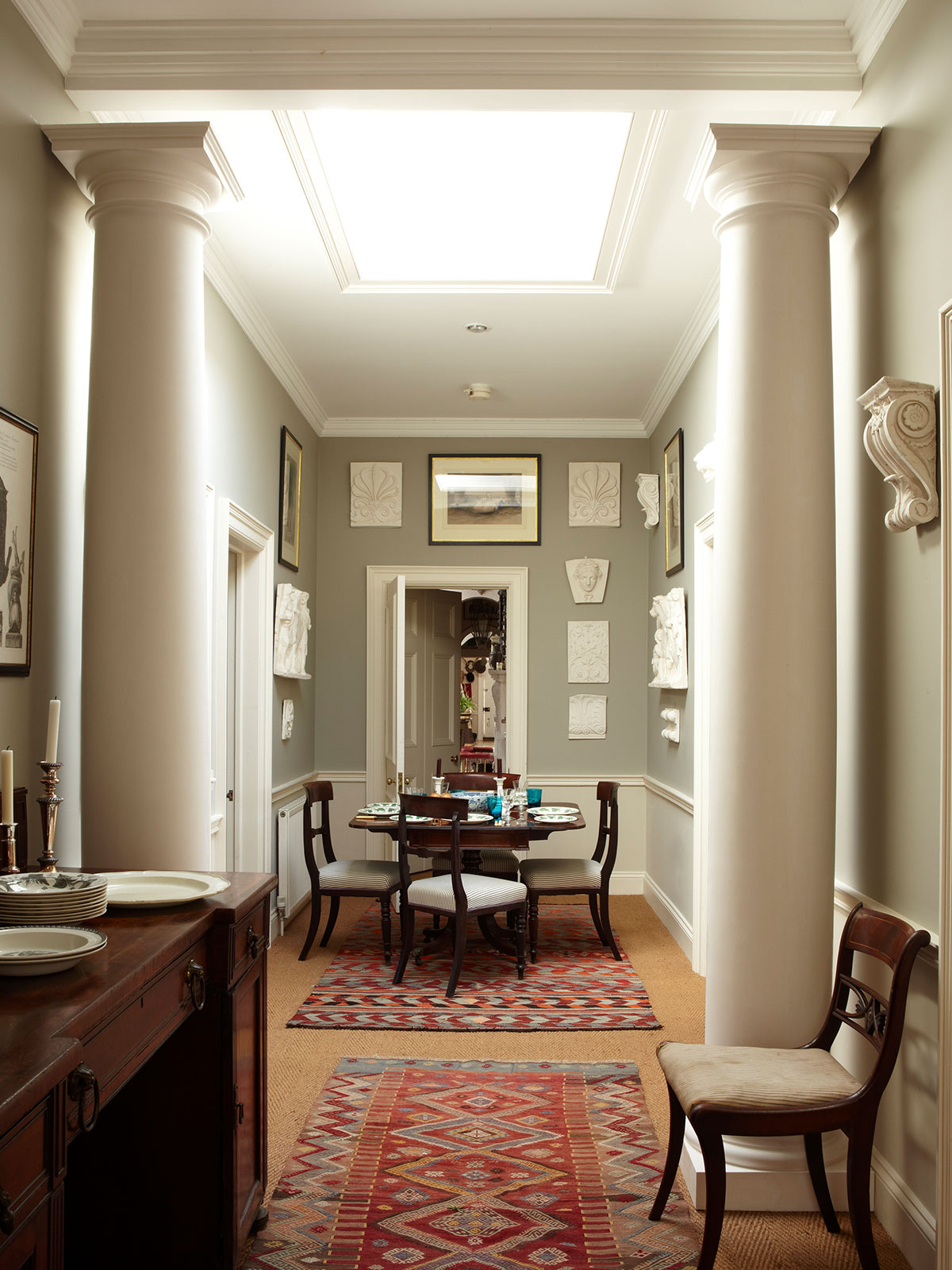 Classical dining space with white columns, grey-green walls, and patterned rugs.