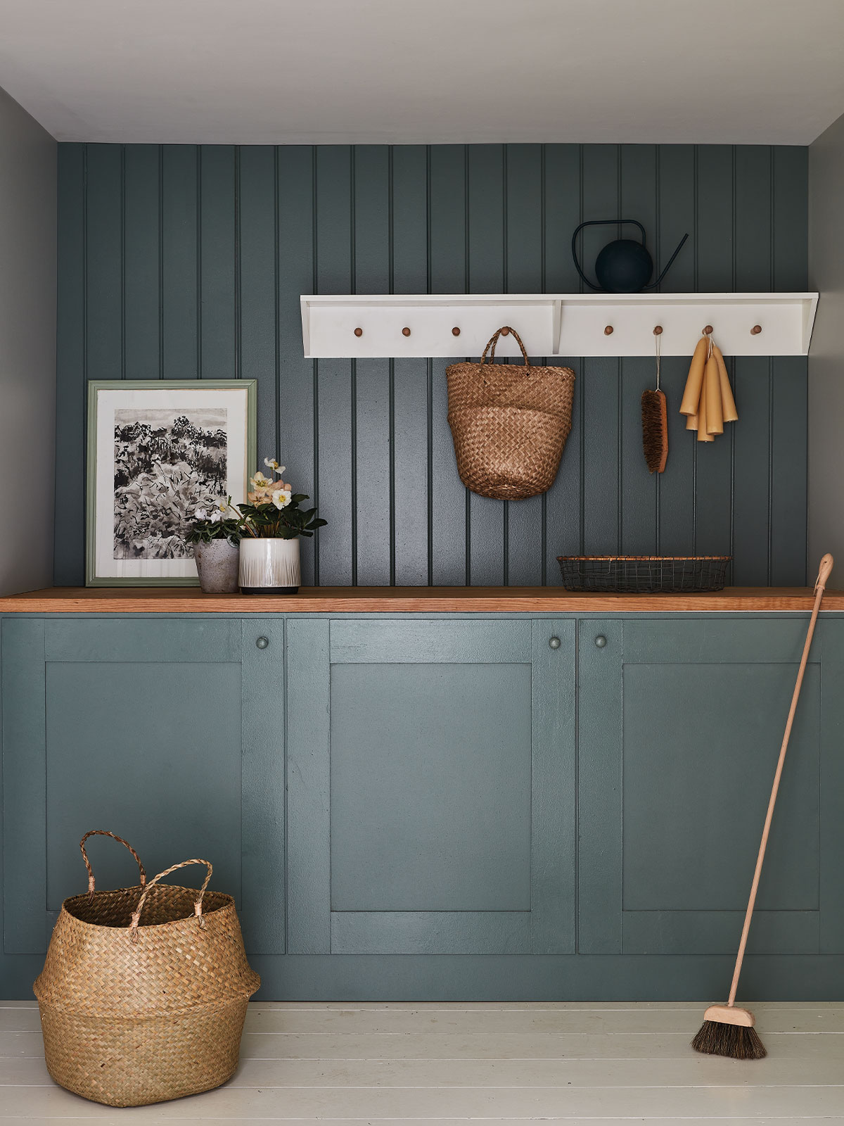 Teal cabinetry with wooden top, woven baskets, and hanging household items.