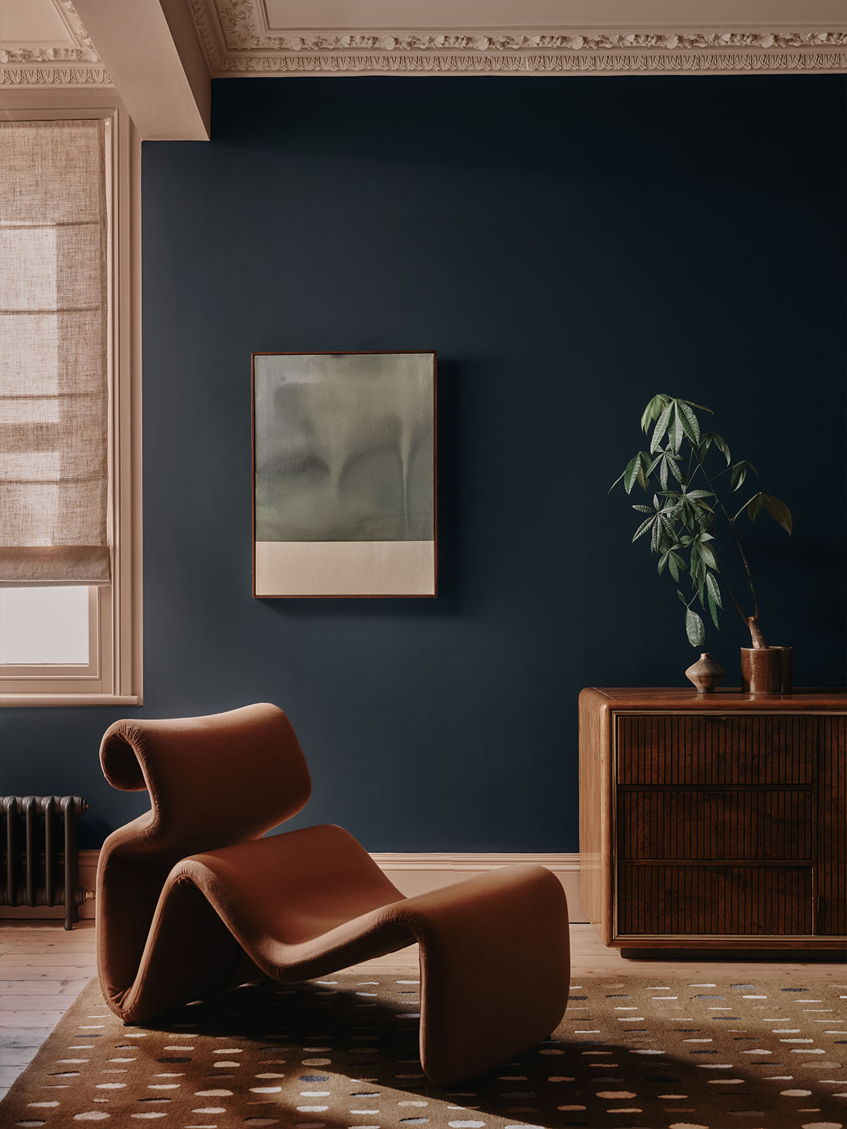 Deep blue living space with sculptural brown chair, abstract artwork, and wooden furniture.