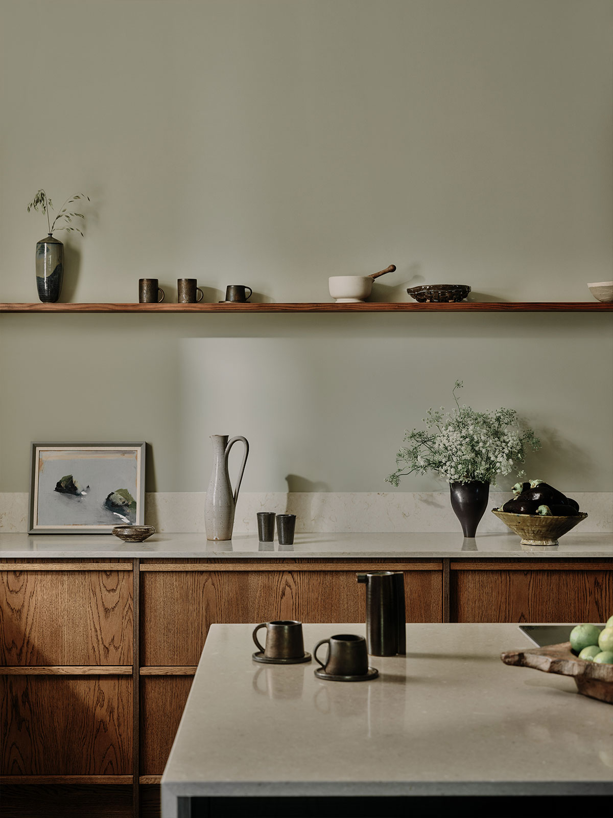 Soft green kitchen with wooden cabinets, stone worktops, and simple ceramic decor.