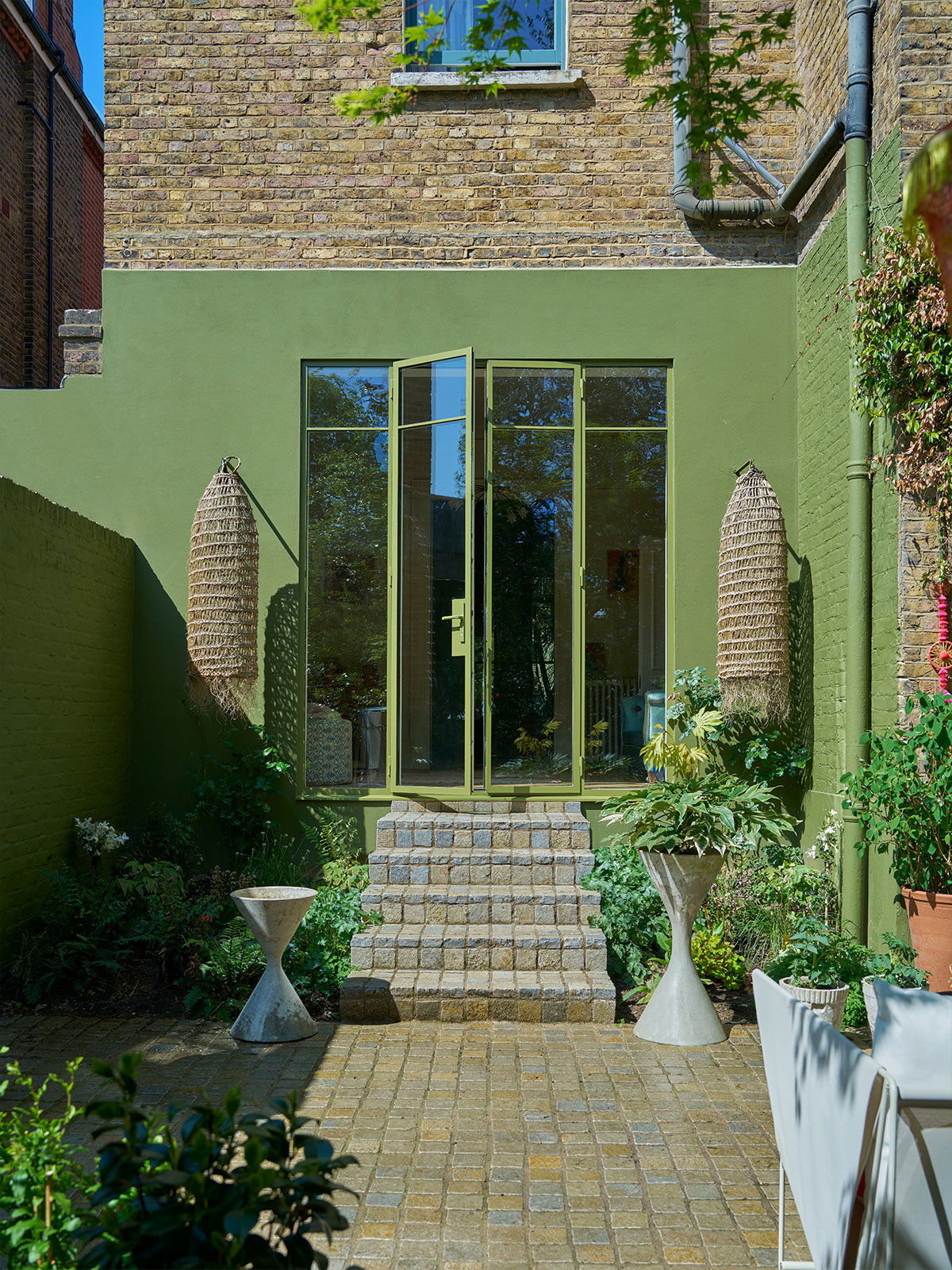 Olive green exterior with brick walls, stone steps, and lush garden plants.