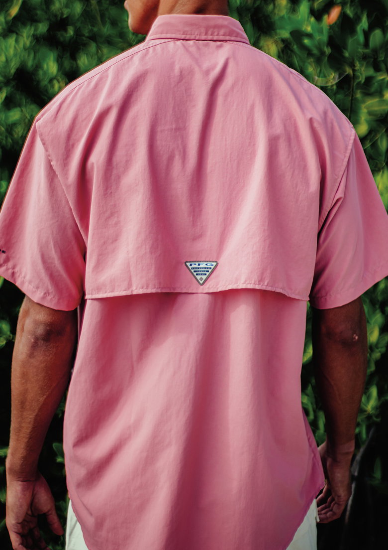 A man facing away wearing a bright pink fishing shirt.