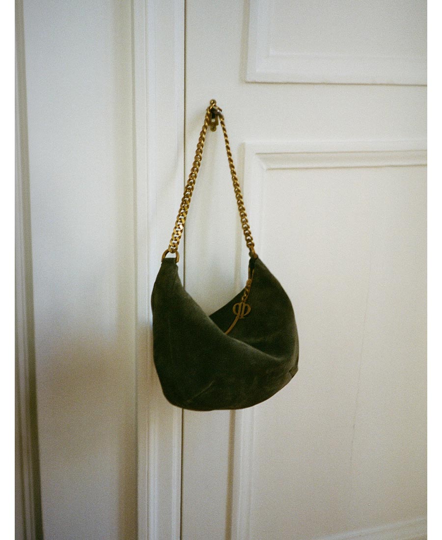 A dark green suede shoulder bag with a gold chain strap hangs from a door knob.
