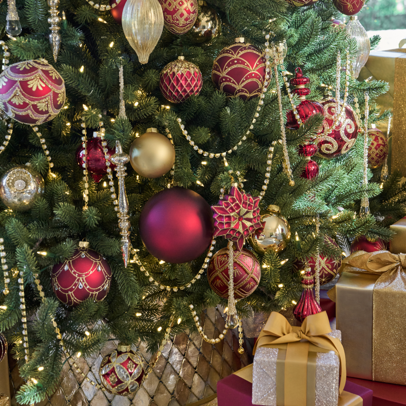 Close-up of a Christmas tree decorated with red, gold, and silver ornaments, beaded garlands, and wrapped presents.