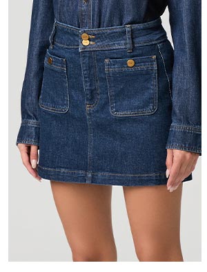 Closeup image of a woman wearing a blue denim skirt with front patch pocket detail.