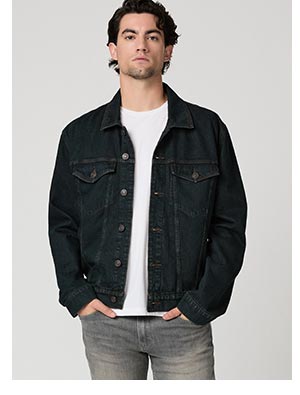 A man wearing a dark blue denim jacket, white tee and grey jeans.