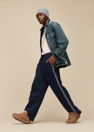 A model in a studio wearing a denim jacket, dark trousers and UGG trainers