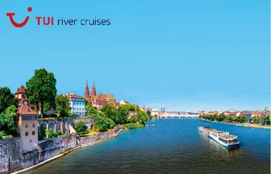 River cruise ship sailing past a scenic European riverside city beneath a clear blue sky.