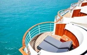 Private sun loungers on a cruise ship deck overlooking bright blue sea.