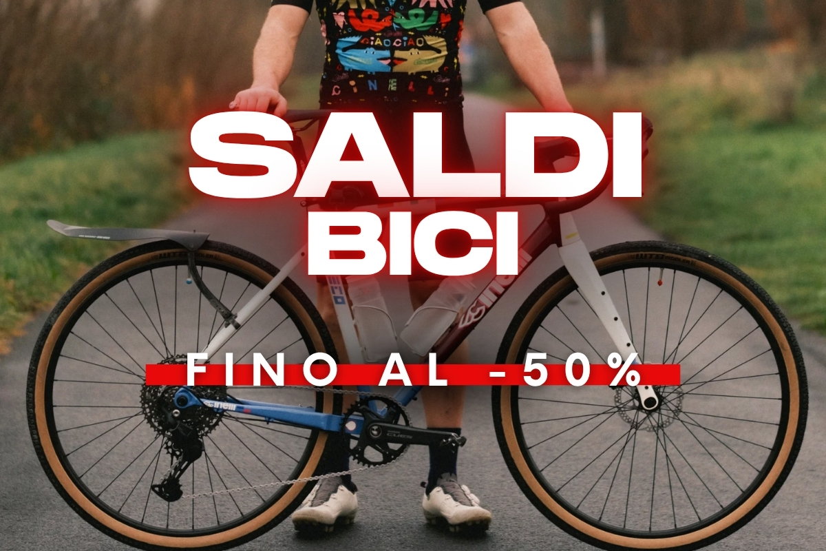 Promotional poster of a person holding a road bike on a path with bold text 'Saldi Bici fino al -50%' advertising bike sale