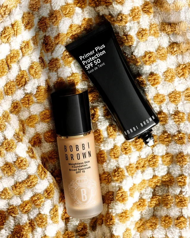 Primer Plus Protection SPF 50 and Weightless Skin Foundation SPF 15 arranged on textured cream fabric with golden dots.