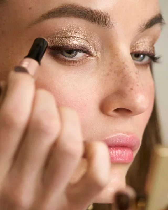 Close-up of a woman's face and hand with Crystal Eyes Shadow Stick being applied.