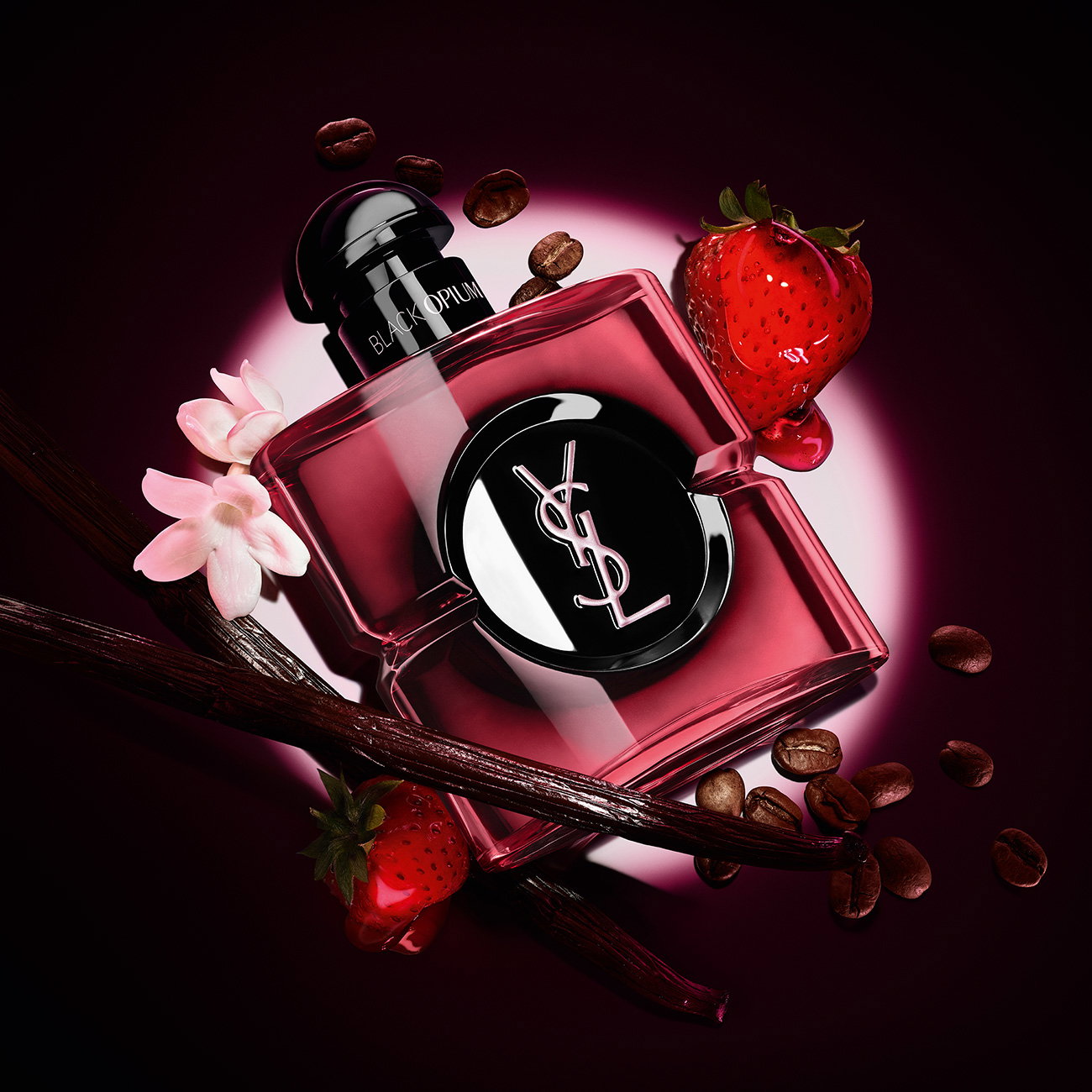 A translucent cherry-red YSL Black Opium fragrance bottle surrounded by coffee beans, vanilla pods, red strawberries, and white flowers under a spotlight.