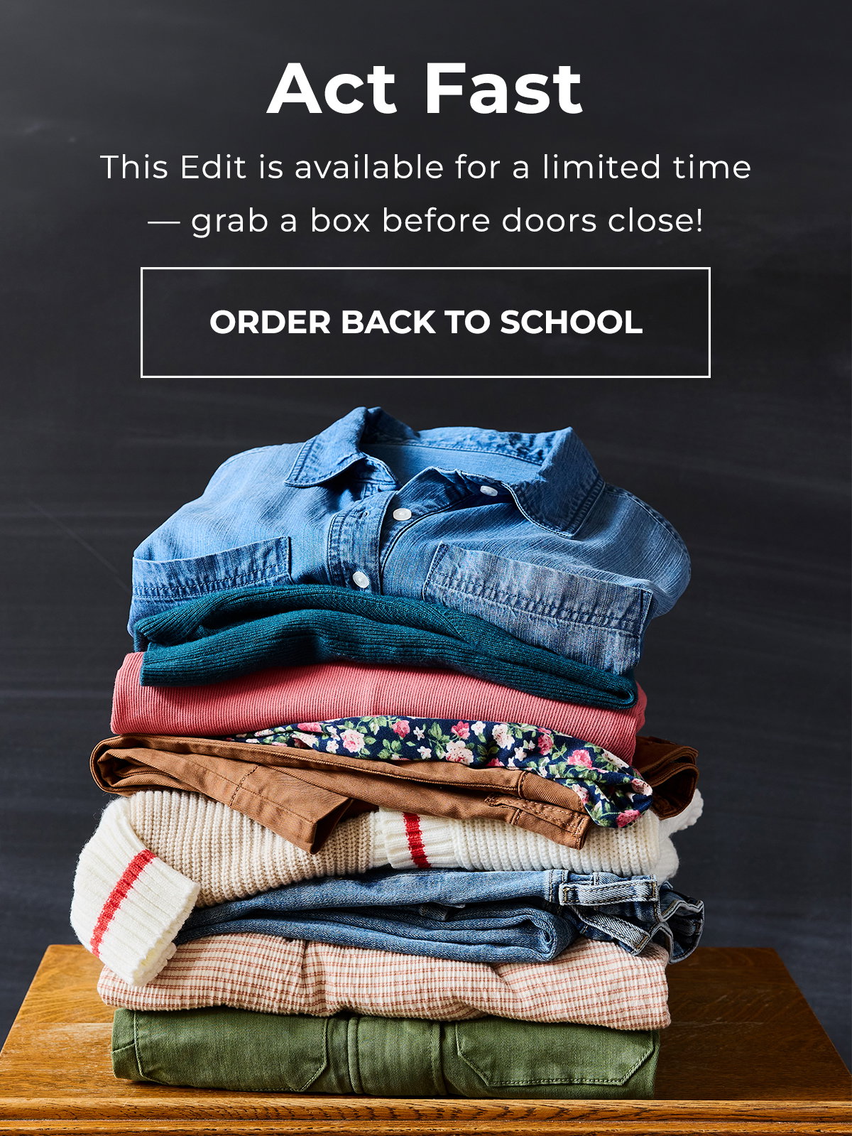 Folded back to school clothes stacked on a table against a dark chalkboard.